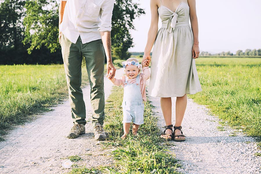 Personal Insurance - Mother and Father Hold Their Baby's Hands in a Field Along a Dirt Road