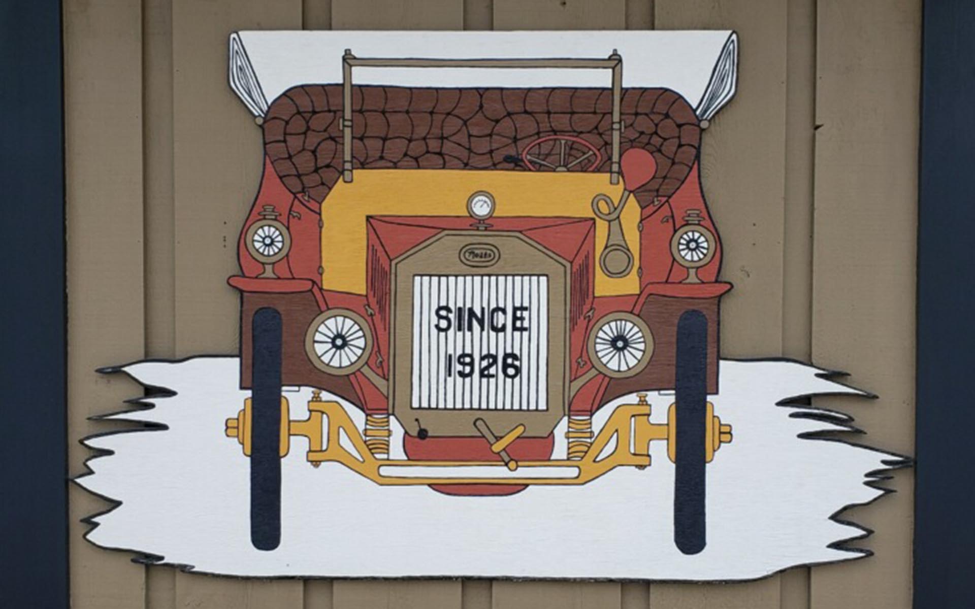 Homepage - A Wooden Sign With a Hand Painted Old-Fashioned Car, With the Words Since 1926 Written on the Grill